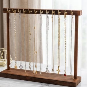 May include: A wooden jewelry display stand with multiple necklaces hanging from it. The stand is a dark brown color and has a rectangular base. The necklaces are various lengths and feature different pendants, including a sun, a cross, and a butterfly.