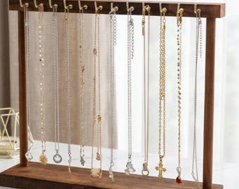 Op de afbeelding: Een donkerhouten sieradenstandaard met meerdere kettingen eraan. De standaard heeft een rechthoekige basis. De kettingen zijn van verschillende lengtes en hebben verschillende hangers, waaronder een zon, een kruis en een vlinder.