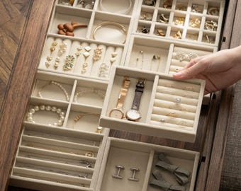 Op de afbeelding: Een houten sieraden organizer met meerdere compartimenten gevuld met diverse sieraden. De organizer bevat armbanden, kettingen, oorbellen, ringen en twee horloges. De compartimenten zijn bekleed met een zachte, beige stof.