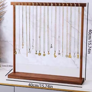 Op de afbeelding: Een houten kettingdisplaystandaard, 40 cm breed en 7,5 cm diep, met talrijke kettingen met diverse hangerontwerpen. De standaard is gemaakt van donker hout en heeft een horizontale balk met kleine pinnen om de kettingen op te hangen.