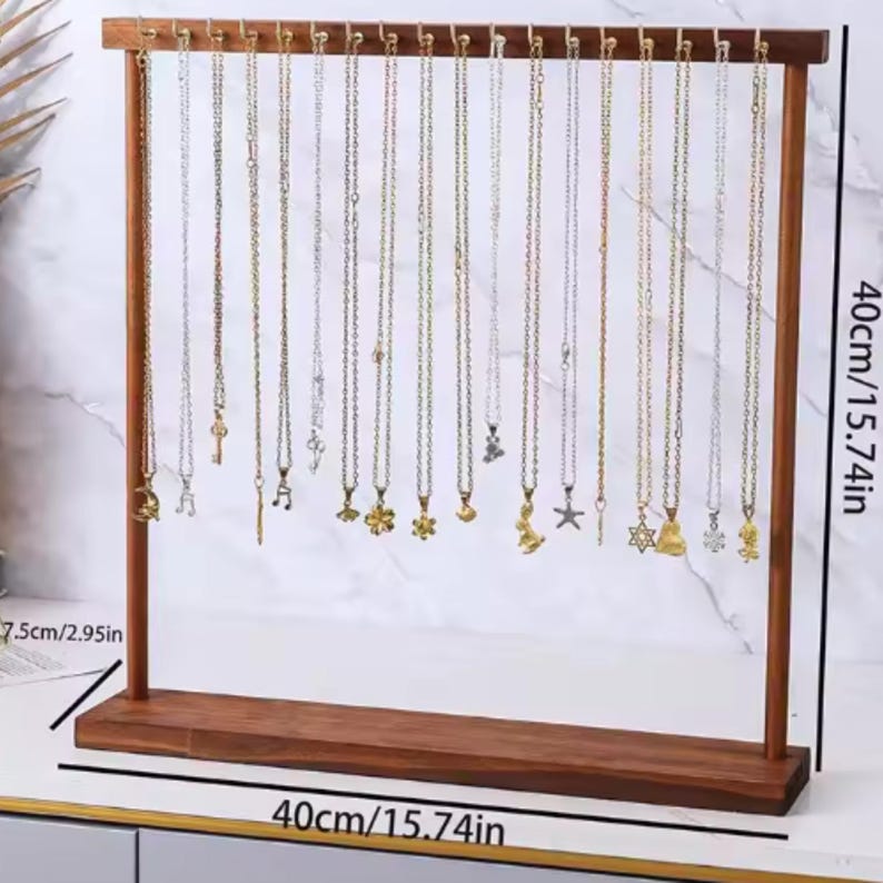 Op de afbeelding: Een houten kettingdisplaystandaard, 40 cm breed en 7,5 cm diep, met talrijke kettingen met diverse hangerontwerpen. De standaard is gemaakt van donker hout en heeft een horizontale balk met kleine pinnen om de kettingen op te hangen.