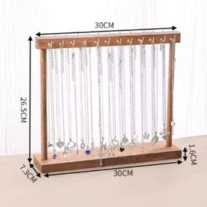 Op de afbeelding: Een houten sieradenstandaard, 30 cm breed en 26,5 cm hoog, met haken voor kettingen. De standaard is gemaakt van bruin hout en bevat veel zilveren kettingen met verschillende hangers. De basis is 7,3 cm diep en 1,6 cm hoog.