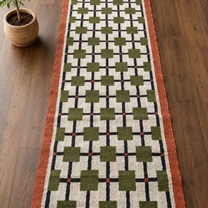 May include: A rectangular runner rug featuring a repeating grid pattern of olive green squares connected by black lines and small orange accents on a cream background, framed by a solid orange border with dark brown fringe at both ends.
