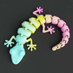May include: A multi-coloured articulated lizard toy in pastel shades of yellow, pink, and blue. The toy is made of connected segments, allowing it to be posed. The lizard has a rounded head, four legs with five toes each, and a curved tail. The background is a dark grey.