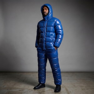Puede incluir: Un mono acolchado de color azul brillante, con acabado de alto brillo, cremallera frontal completa, mangas largas y capucha incorporada. La prenda presenta un acabado reflectante y una estructura aislante acolchada con costuras horizontales.