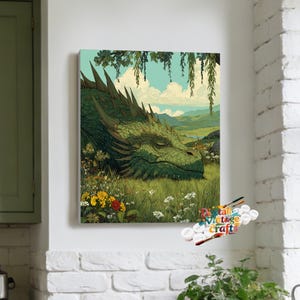 May include: A rectangular paint-by-numbers canvas featuring a large green dragon resting in a field of wildflowers and tall grass. The background shows rolling hills, a light blue sky with white clouds, and hanging willow branches. Text reads Digital Vintage Crafts.