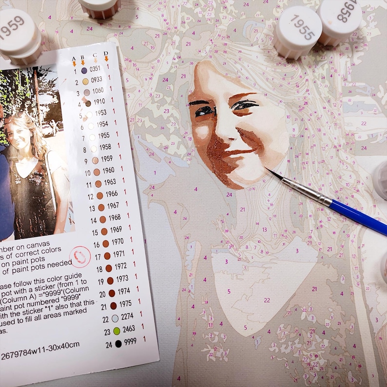 May include: A paint-by-numbers kit on canvas featuring a portrait of a person, accompanied by a color guide with numbered stickers and small paint pots. A thin paintbrush with a blue handle rests on the canvas, which measures 30x40 cm.