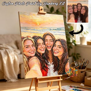 May include: A custom photo paint by numbers kit displayed on a wooden easel. The canvas features an oil-style painting of four smiling individuals at a beach during sunset, matching the small reference photo shown in the upper right corner.