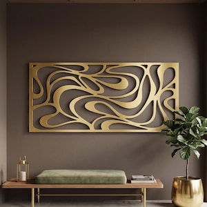 Può includere: Un'opera d'arte da parete rettangolare in metallo color oro caratterizzata da un intricato motivo ritagliato, astratto e fluido. Il design è composto da linee curve, lisce e interconnesse che creano un effetto visivo continuo, organico e fluido.