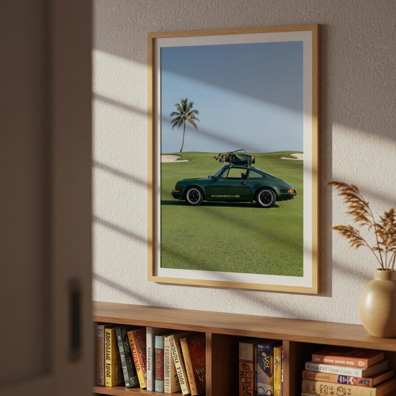 Puede incluir: Impresi&oacute;n enmarcada de un coche deportivo Porsche verde oscuro estacionado en un campo de golf. El coche tiene una bolsa de golf encima. El fondo incluye una palmera, cielo azul y hierba verde. La palabra "PORSCHE" es visible.