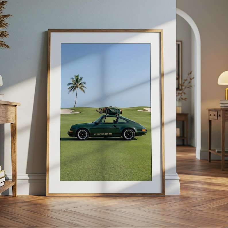 Puede incluir: Impresi&oacute;n enmarcada que presenta un coche deportivo Porsche verde oscuro estacionado en un campo de golf. El coche tiene una bolsa de golf en el techo. El fondo incluye una palmera, trampas de arena y un cielo azul. La palabra "PORSCHE" es visible.