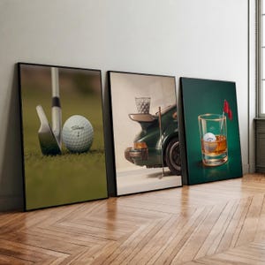 May include: Three framed wall art prints featuring golf themes. The first shows a Titleist golf ball and club on green grass. The second displays a dark green sports car with a basket of golf balls. The third depicts a golf ball in a glass of whiskey.