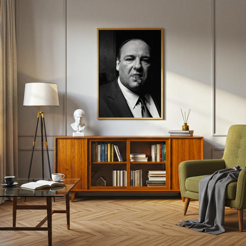 K&ouml;nnte beinhalten: Ein gerahmtes Schwarz-Wei&szlig;-Portr&auml;t eines Mannes im Anzug, der eine Zigarre raucht, an einer Wand &uuml;ber einem h&ouml;lzernen Sideboard. Das Kunstwerk zeigt ein kontrastreiches, monochromes Bild einer Person mit ernstem Ausdruck in einem goldenen Rahmen.
