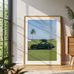 Puede incluir: Impresi&oacute;n enmarcada que presenta un coche deportivo Porsche verde oscuro estacionado en un campo de golf. El coche tiene un portaequipajes en la parte superior. Una palmera y cielo azul en el fondo. La impresi&oacute;n est&aacute; en un marco de madera.