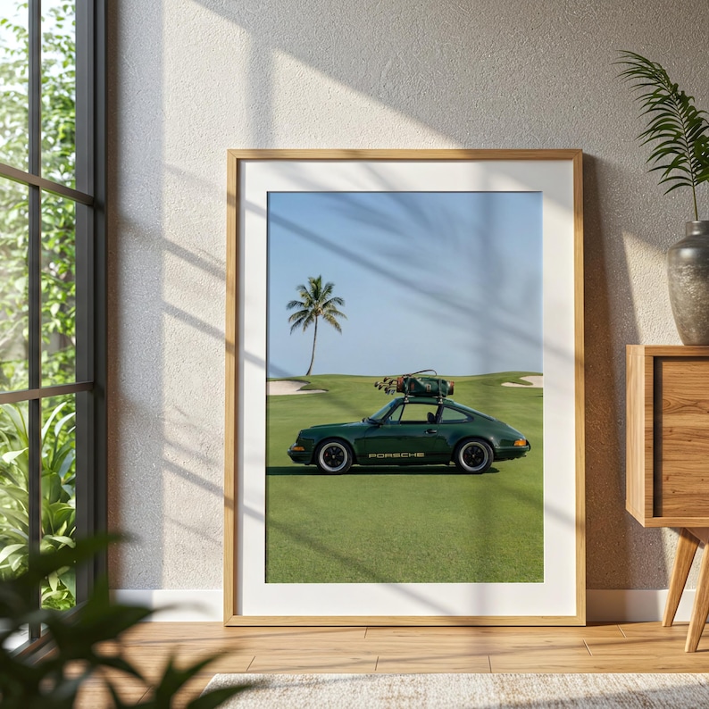 Puede incluir: Impresi&oacute;n enmarcada que presenta un coche deportivo Porsche verde oscuro estacionado en un campo de golf. El coche tiene un portaequipajes en la parte superior. Una palmera y cielo azul en el fondo. La impresi&oacute;n est&aacute; en un marco de madera.