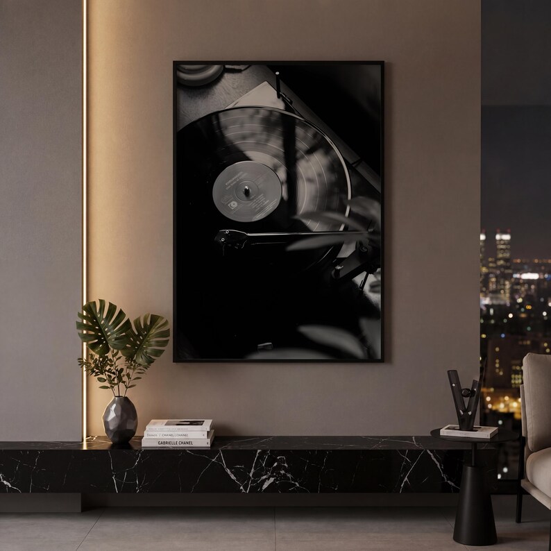 Op de afbeelding: Een ingelijste zwart-wit wandkunstprint met een vinylplaat op een platenspeler. Het kunstwerk heeft een compositie met hoog contrast, diepe schaduwen en highlights, waarbij de groeven van de plaat en de toonarm duidelijk zichtbaar zijn.
