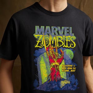 Puede incluir: Una camiseta negra de manga corta con un gráfico de Marvel Zombies. El estampado muestra una mano en descomposición con garras saliendo de una tumba bajo una luna verde. El texto dice: MARVEL ZOMBIES y WOLVERINE IS BACK FROM THE BEYOND...BUB!