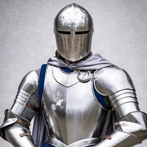 Könnte beinhalten: Eine vollständige Rüstung aus poliertem Stahl, einschließlich Helm, Brustplatte mit Adleremblem und Arm- und Beinschutz. Die Rüstung wird über einer blauen Tunika mit einem Halbmond-Design getragen. Ein grauer Umhang vervollständigt das mittelalterliche Ritterensemble.