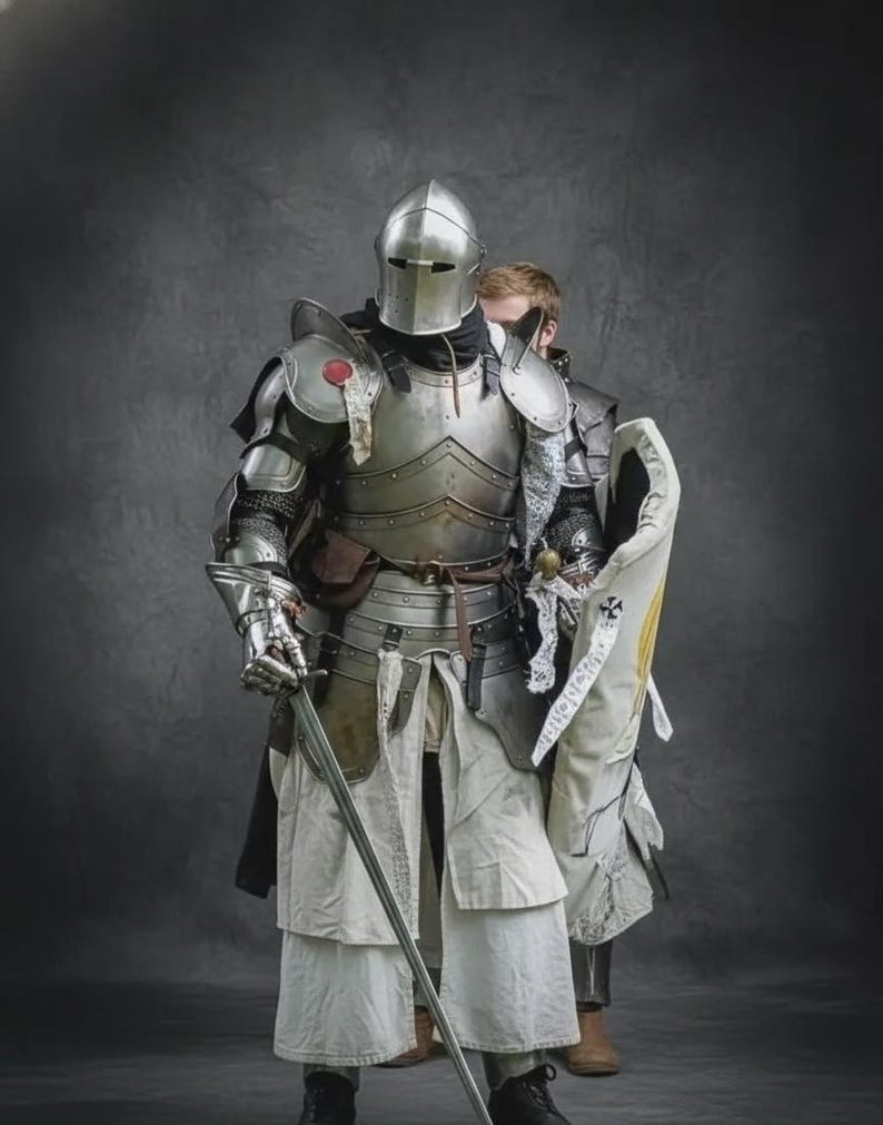 May include: A complete set of medieval armour, including a helmet, chest plate, and leg guards. The silver-coloured armour features detailed craftsmanship and is worn with a white tunic and black boots. A sword is held in the right hand.