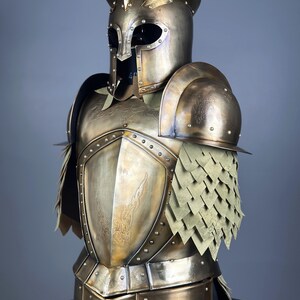 May include: A detailed bronze-colored suit of armor, featuring a helmet with a distinctive crest and eye openings. The breastplate and shoulder guards are adorned with etched designs and rivets. The armor includes layered, scale-like elements.