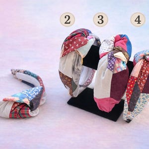 May include: Four colorful fabric headbands with patchwork designs. The headbands feature a variety of patterns and colors, including red, blue, pink, and floral prints. One headband is lying flat, while the others are displayed on a black stand.