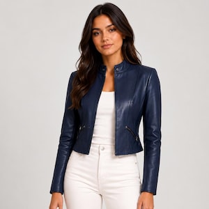 Puede incluir: Una chaqueta de cuero azul marino con cuello mao, cierre de cremallera frontal y dos bolsillos laterales con cremallera en la cintura. La chaqueta se lleva sobre una camiseta blanca lisa y se combina con pantalones blancos, mostrando un corte entallado.