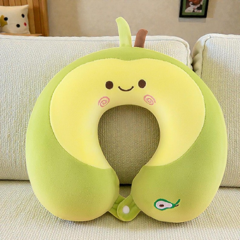 Pode incluir: Uma almofada de viagem em forma de abacate. A almofada em forma de U &eacute; verde claro com um centro amarelo e um rosto sorridente com bochechas rosadas. Possui um pequeno caule e uma folha no topo e um caro&ccedil;o de abacate na parte inferior.