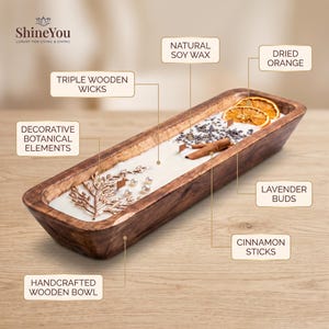 Puede incluir: Un cuenco de madera artesanal largo y rectangular relleno de cera de soja natural blanca con tres mechas de madera. La vela está decorada con rodajas de naranja seca, capullos de lavanda, ramas de canela, perlas blancas y una rama metálica.