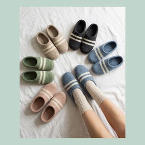 Peut inclure: Diverses pantoufles en laine feutrée de couleurs beige, grise, verte, rose et bleue. Chaque pantoufle est ornée de deux rayures blanches. Une paire est portée avec des chaussettes beiges.