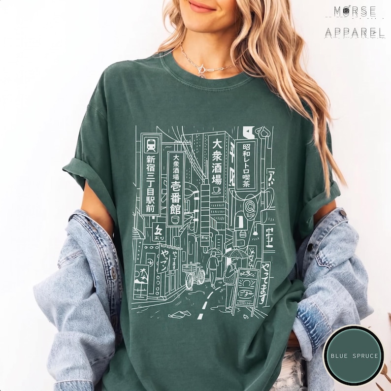 Puede incluir: Una camiseta verde oscuro con un dibujo lineal blanco de una escena callejera japonesa. El dise&ntilde;o incluye edificios, letreros y personas. El texto de la camiseta incluye caracteres japoneses y las palabras "MORSE APPAREL" y "BLUE SPRUCE".