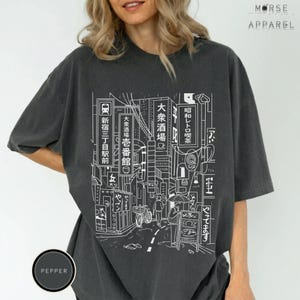 Puede incluir: Camiseta gris oscuro con un dibujo lineal blanco de una escena callejera japonesa con edificios y letreros. La camiseta tiene el texto "MORSE APPAREL" y "PEPPER" impreso.