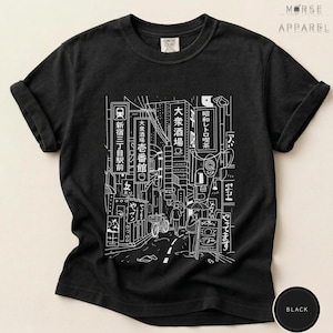 Puede incluir: Camiseta negra con un dibujo lineal blanco que representa una escena callejera japonesa, con letreros, edificios y figuras. El dise&ntilde;o incorpora texto japon&eacute;s. La camiseta tiene las mangas enrolladas y la marca "MORSE APPAREL" es visible.