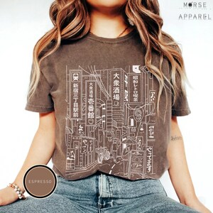 Puede incluir: Camiseta color espresso con un dibujo lineal blanco de un paisaje urbano japon&eacute;s y texto en japon&eacute;s. La camiseta tiene cuello redondo y mangas cortas. La marca "MORSE APPAREL" est&aacute; impresa en la parte superior derecha.