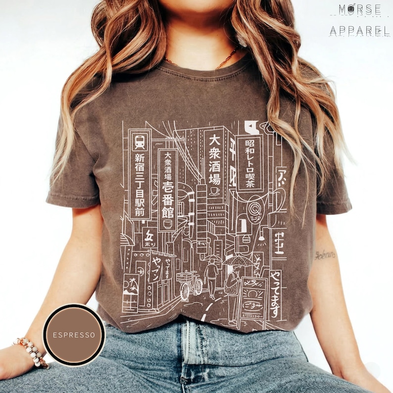 Puede incluir: Camiseta color espresso con un dibujo lineal blanco de un paisaje urbano japon&eacute;s y texto en japon&eacute;s. La camiseta tiene cuello redondo y mangas cortas. La marca "MORSE APPAREL" est&aacute; impresa en la parte superior derecha.