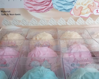 May include: A display box containing multiple squishy cream roll toys in pink, blue, and white colours. The packaging features the text Soft Touch, Squishy Cream Roll, and states the material is safe and non-toxic. Each toy is individually boxed.