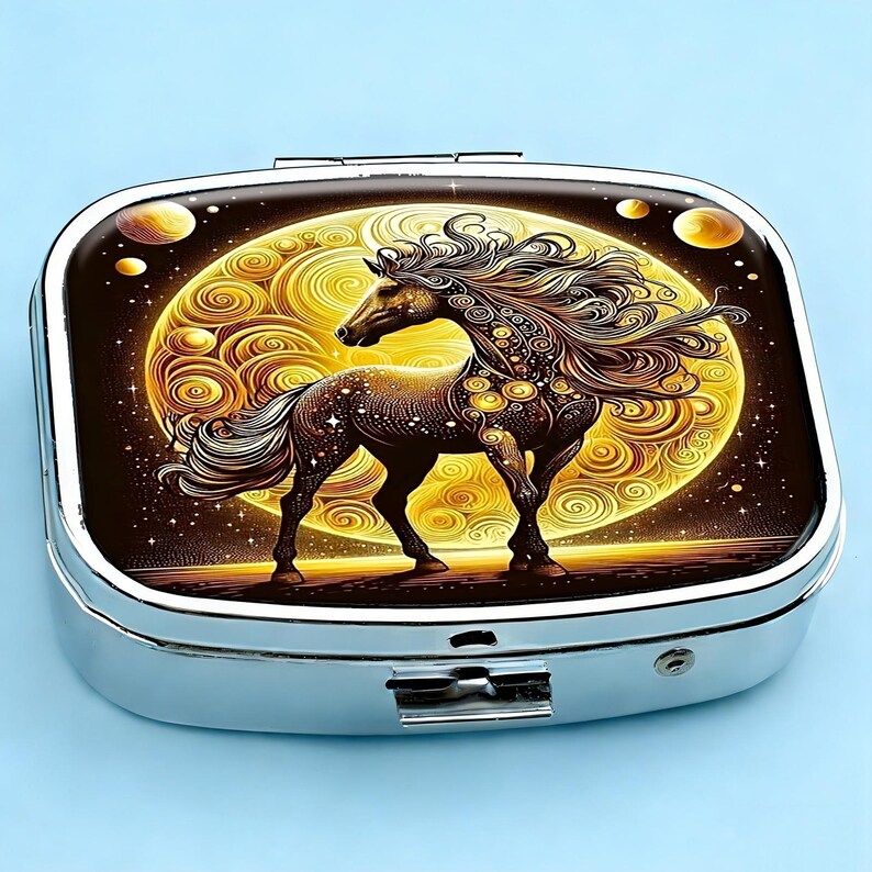 K&ouml;nnte beinhalten: Eine silberne Pillendose mit einer detaillierten Illustration eines Pferdes vor einem goldenen Mondhintergrund. Das Pferd ist braun mit flie&szlig;ender M&auml;hne und Schweif, verziert mit dekorativen Elementen. Der Hintergrund zeigt ein wirbelndes Muster und himmlische Akzente.