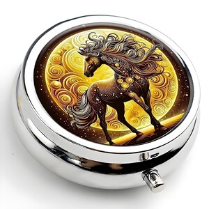 K&ouml;nnte beinhalten: Eine silberne Pillendose mit einer detaillierten Illustration eines Pferdes vor einem goldenen, wirbelnden Hintergrund. Das Pferd ist braun mit flie&szlig;ender M&auml;hne und Schweif, und der Hintergrund &auml;hnelt einem Vollmond.