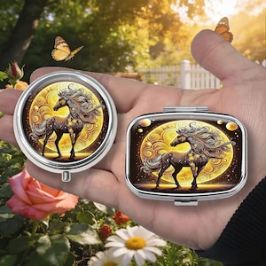 K&ouml;nnte beinhalten: Zwei silberne Pillendosen, eine runde und eine rechteckige, jeweils mit einer detaillierten Illustration eines Pferdes vor einem goldenen, wirbelnden Hintergrund. Das Pferd ist braun mit flie&szlig;ender M&auml;hne und Schweif. Die Dosen werden in einer Hand gehalten, mit Schmetterlingen und Blumen im Hintergrund.