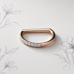 Könnte beinhalten: Ein Creolenring aus Roségold mit einem geraden Stiftverschluss und einem gebogenen Segment, das mit acht kleinen, klaren, rund geschliffenen Steinen besetzt ist. Das Metall hat eine polierte Oberfläche und kombiniert ein glattes Band.