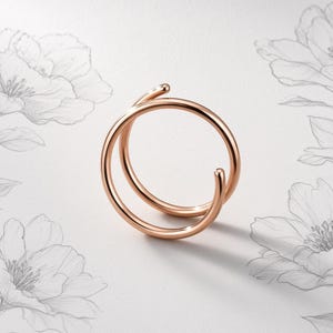 Può includere: Un anello in oro rosa con un design a doppio anello e una finitura liscia e lucida. L'anello è composto da due fasce circolari continue e sovrapposte che creano un aspetto stratificato, mostrando una lucentezza metallica e bordi arrotondati.