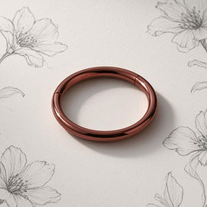 May include: A smooth, circular hoop ring with a polished copper-toned finish. The ring features a seamless, continuous design with a hinged segment for opening and closing, presented as a simple, solid metal band with a reflective surface.