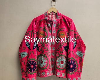May include: A bright pink jacket featuring intricate floral embroidery in shades of teal, dark blue, and orange. The garment has a high collar, long sleeves, and a front zipper closure. The text Saymatextile is printed across the center.
