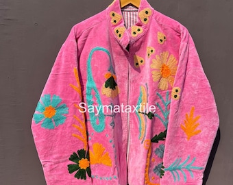 May include: A pink jacket with floral embroidery in teal, orange, and yellow. The jacket has a high collar and long sleeves. The text "Saymataxtile" is visible on the front of the jacket.