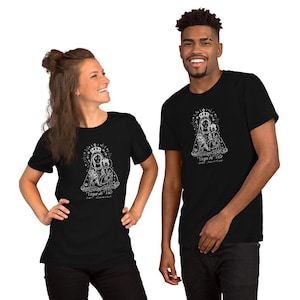 May include: Black t-shirts featuring a white graphic of a religious figure with a crown, halo, and child. The text "Virgen del Valle" and other text is below the image. The t-shirts are worn by two people.