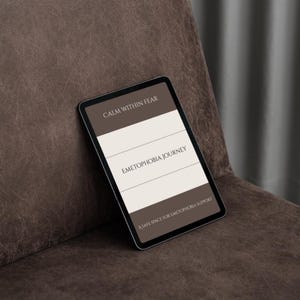 May include: A digital tablet displaying text on a brown and white background. The text reads "CALM WITHIN FEAR", "EMETOPHOBIA JOURNEY", and "A SAFE SPACE FOR EMETOPHOBIA SUPPORT". The tablet is resting on a brown leather surface.