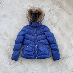 Könnte beinhalten: Eine leuchtend blaue Steppjacke mit einer Kapuze mit Kunstfellbesatz. Die Jacke hat einen hohen Kragen, Knopfverschlüsse und zwei Vordertaschen. Ein kleines Logo ist auf dem Ärmel sichtbar. Dieser Wintermantel ist auf Wärme und Stil ausgelegt.