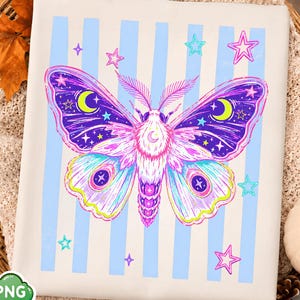 May include: A white t-shirt featuring a graphic of a large moth with purple, pink, and blue wings decorated with yellow crescent moons and stars. The background of the design consists of vertical light blue stripes and several small pink and blue stars.