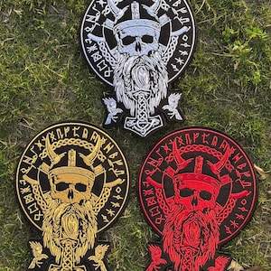 Könnte beinhalten: Drei gestickte Aufnäher mit Wikinger-Motiven. Jeder Aufnäher zeigt einen Schädel mit Hörnerhelm, langem Bart und Hammelsymbol. Die Aufnäher sind in Weiß, Gold und Rot gehalten, mit kreisförmigen Rändern und Runentext.