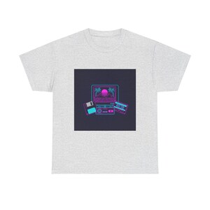 Puede incluir: Camiseta gris claro con un gráfico retro. El diseño presenta un ordenador portátil, un disquete y una cinta de cassette en azul neón y rosa. La pantalla del portátil muestra una puesta de sol con palmeras.