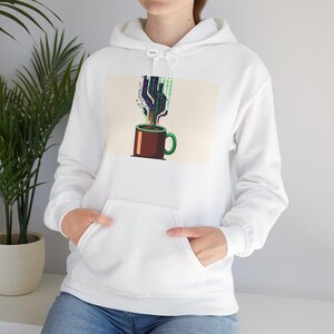 Peut inclure: Sweat à capuche blanc avec une poche avant. Le graphisme représente une tasse à café marron avec une anse verte, d'où s'échappent des codes binaires et des motifs de circuits imprimés. Le motif est posé sur un fond beige.